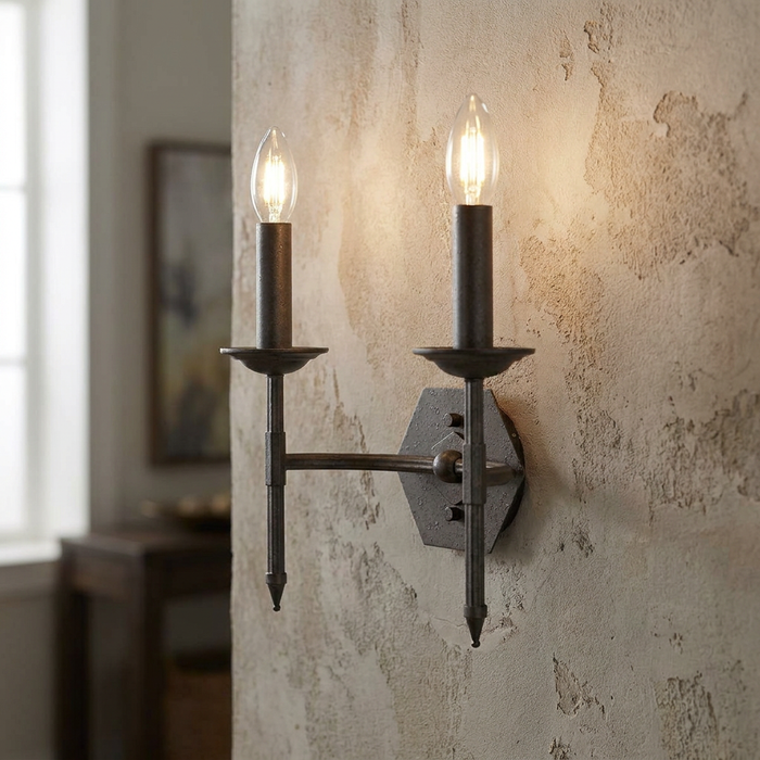 A two-light rustic iron wall sconce with candle-style bulbs mounted on a textured beige plaster wall.