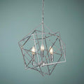 Three-light chrome geometric cube ceiling pendant with illuminated candle bulbs against a blue-green background.