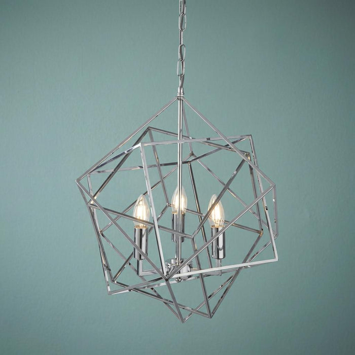 Three-light chrome geometric cube ceiling pendant with illuminated candle bulbs against a blue-green background.