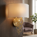 Aged brass wall light with a decorative ring design and a white fabric shade mounted on a wooden wall.