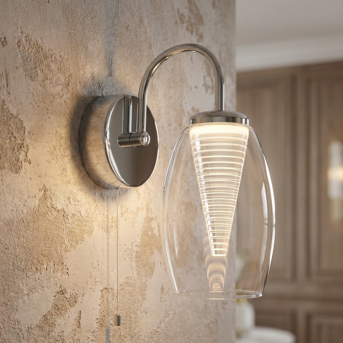 Chrome kitchen wall light with a clear oval glass shade and a glowing conical interior on a textured wall.