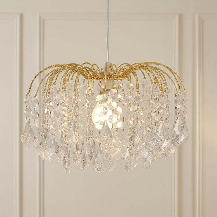 Elegant brass pendant lamp shade with cascading clear crystal droplets, illuminated against a paneled wall.