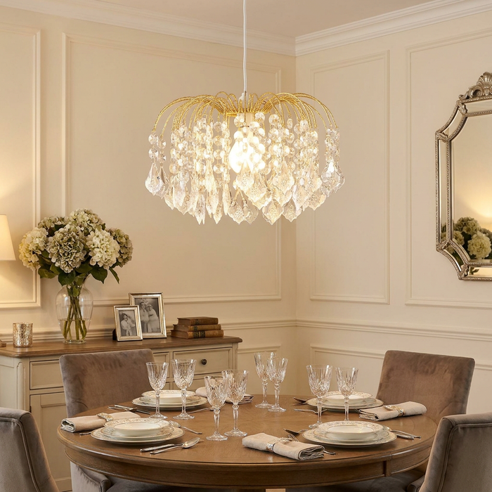 Dacia brass and crystal pendant lamp shade hanging over an elegantly set dining table in a neutral-toned room.
