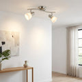Two-light nickel bar spotlight with white glass shades mounted on a ceiling in a minimalist living room.