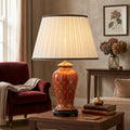Datai terracotta and gold ceramic table lamp with a pleated white shade on a wooden table in a cozy living room.