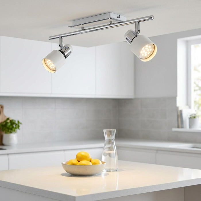 Chrome and white two-light bar spotlight fixture mounted on a modern kitchen ceiling above a white island.