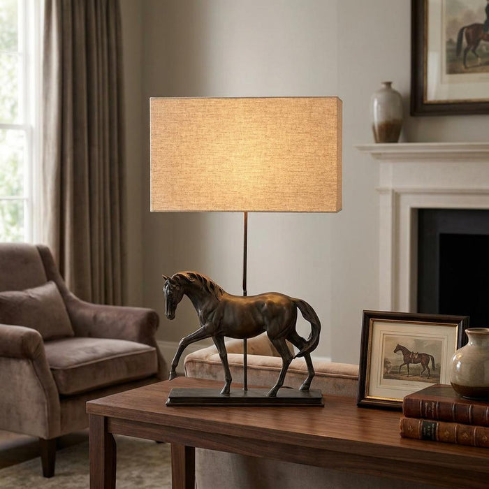 Bronze horse sculpture table lamp with a rectangular natural shade on a wooden table in a cozy living room.
