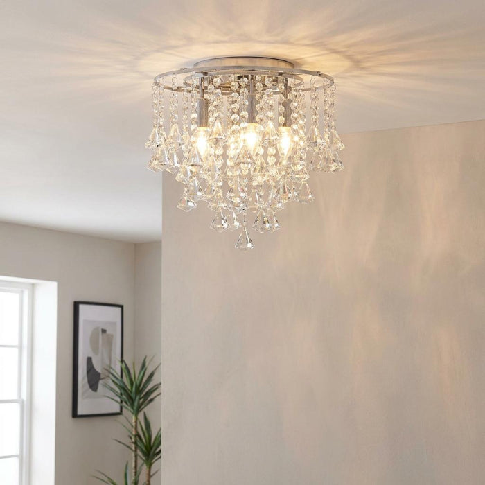A chrome and crystal flush ceiling light illuminating a living room with warm, patterned shadows.