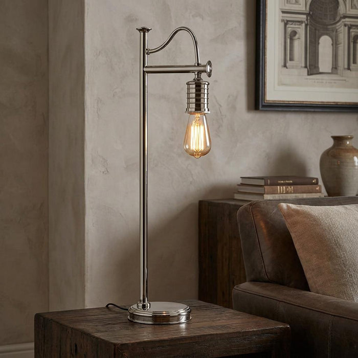 Polished nickel Douille table lamp with an exposed vintage bulb on a wooden side table next to a leather sofa.