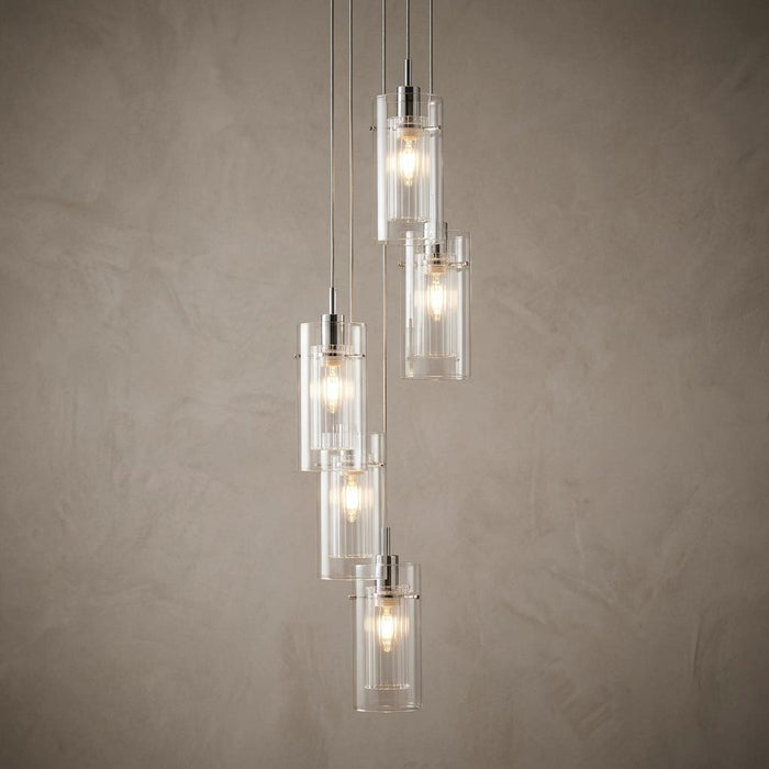 Cascading five-light pendant with chrome accents and double glass cylinders against a neutral textured wall.