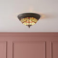 Durham flush Tiffany ceiling light with warm stained glass patterns mounted on a white ceiling above pink paneling.