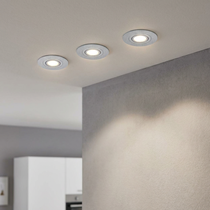 Set of three round aluminum recessed spotlights in a ceiling illuminating a grey textured wall.