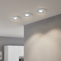 Set of three round aluminum recessed spotlights in a ceiling illuminating a grey textured wall.
