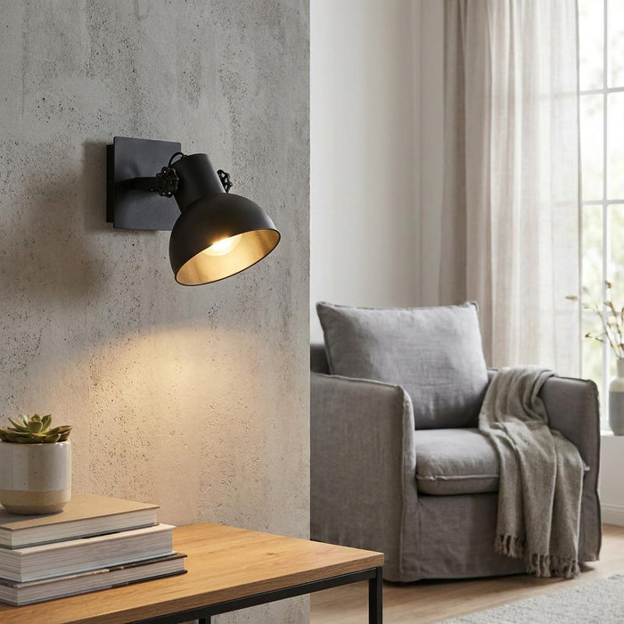 Industrial black wall spotlight with a warm gold interior lit on a textured concrete wall in a living room.