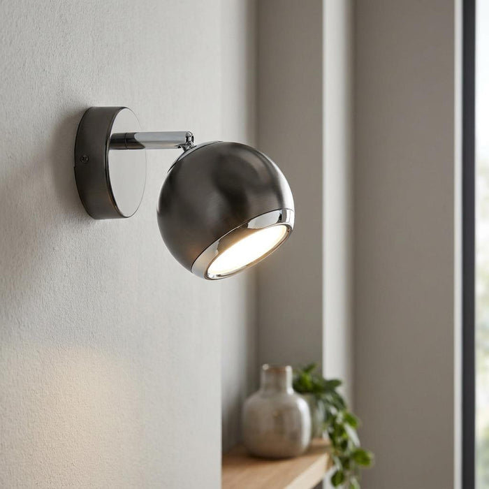 Eglo Bimeda black nickel and chrome wall spotlight mounted on a textured wall, emitting a warm glow.
