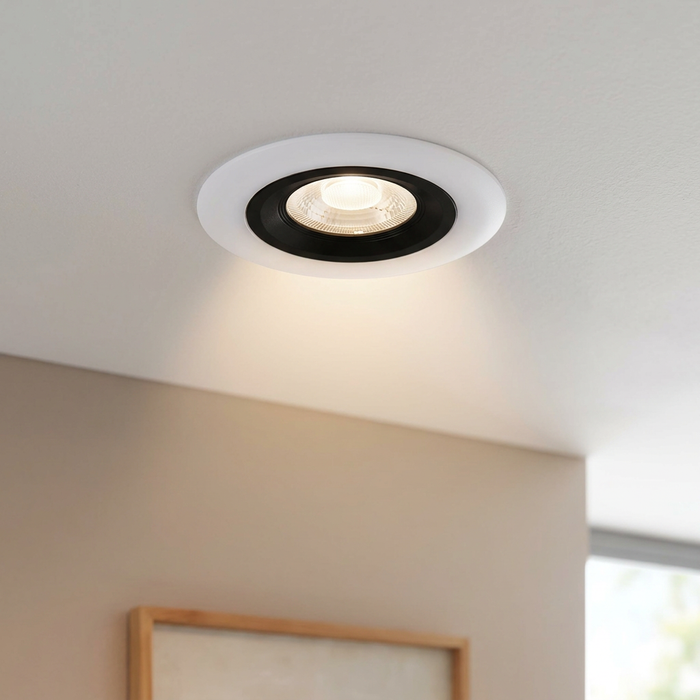 Round white recessed ceiling spotlight with a black inner ring illuminated on a white ceiling.