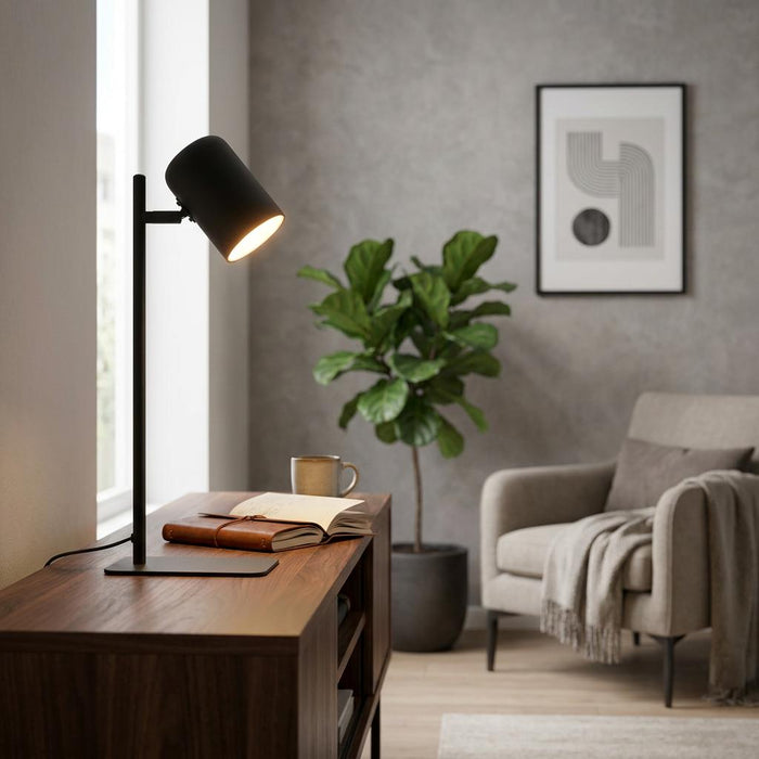 Modern black metal table lamp illuminating an open notebook on a wooden sideboard in a cozy living room.