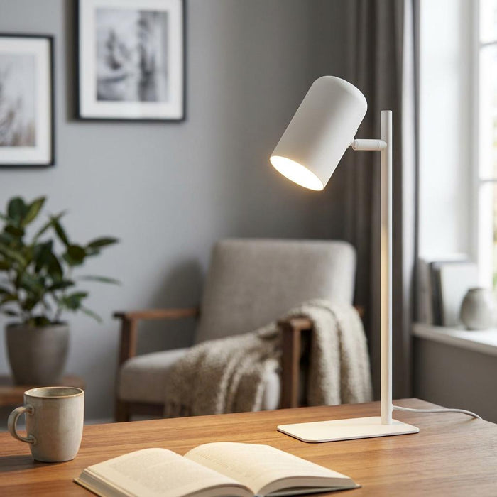 Sleek white metal table lamp with an adjustable cylindrical head casting warm light onto a book on a wooden desk.