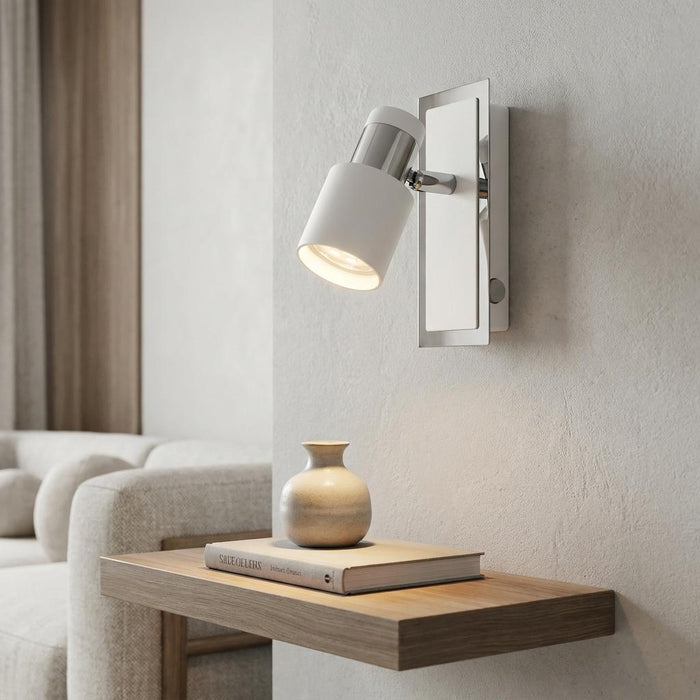 White and chrome adjustable wall spotlight mounted on a textured wall above a wooden shelf with a small vase.