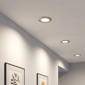 Three brushed nickel recessed LED downlights installed in a white ceiling above framed artwork on a wall.