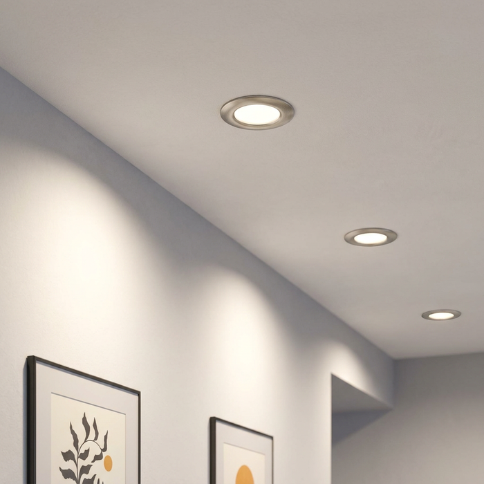 Three brushed nickel recessed LED downlights installed in a white ceiling above framed artwork on a wall.