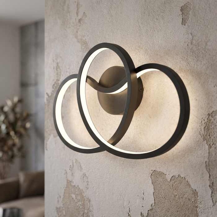 Modern black LED wall light with three overlapping glowing circular rings mounted on a rustic plaster wall.