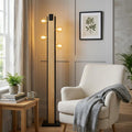 Modern Eglo Layham black and wooden floor lamp with four glowing bulbs next to a white armchair in a living room.