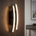 Modern black wall light with two curved glowing plastic crystal bars mounted on a dark wood panel.