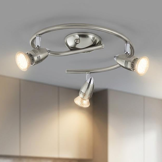 A three-light nickel LED spotlight fixture mounted on a kitchen ceiling above a minimalist white island.
