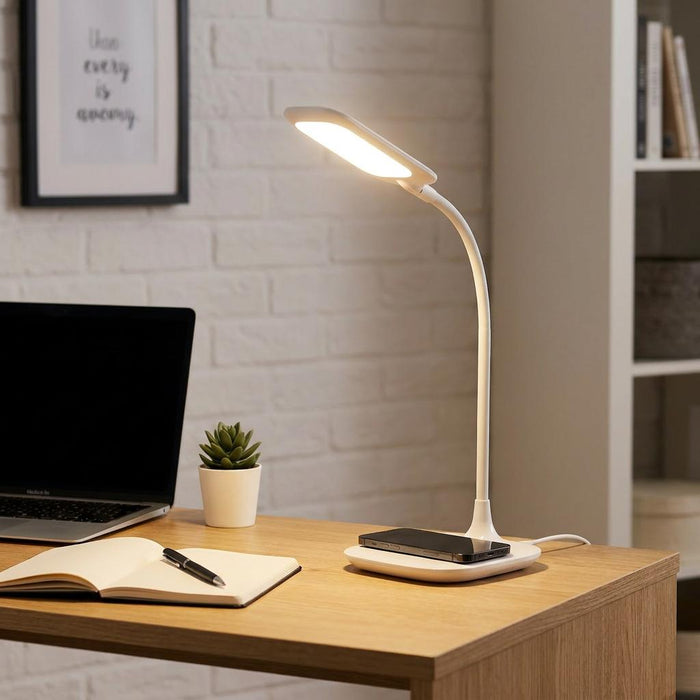 White LED desk lamp with a flexible neck and Qi charging base illuminates a workspace with a laptop and notebook.