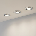 Set of three chrome recessed LED downlights installed in a ceiling, casting a warm glow on a wall.