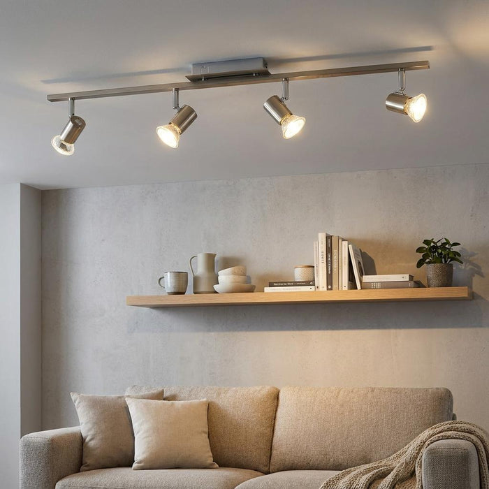 Modern four-light nickel bar spotlight illuminating a contemporary living room with a shelf and sofa.