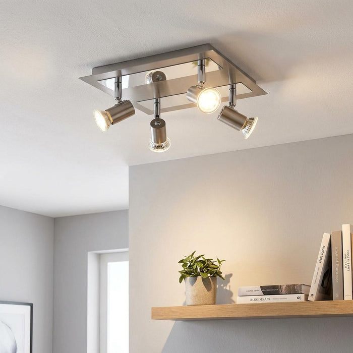 Modern nickel and chrome 4-light plate spotlight mounted on a white ceiling illuminating a shelf below.