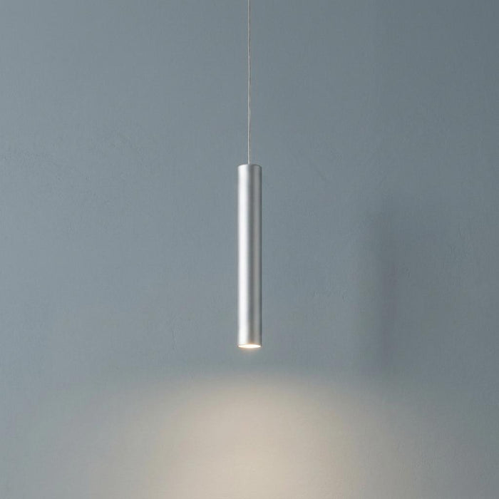 Sleek silver cylindrical LED pendant light hanging against a grey textured wall with a downward glow.