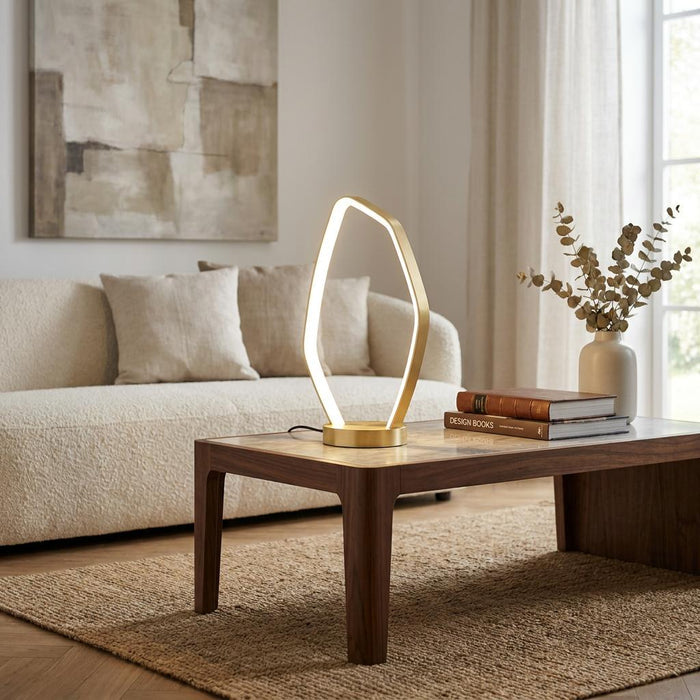 Gold LED table lamp with an organic loop design on a wooden coffee table in a neutral living room.