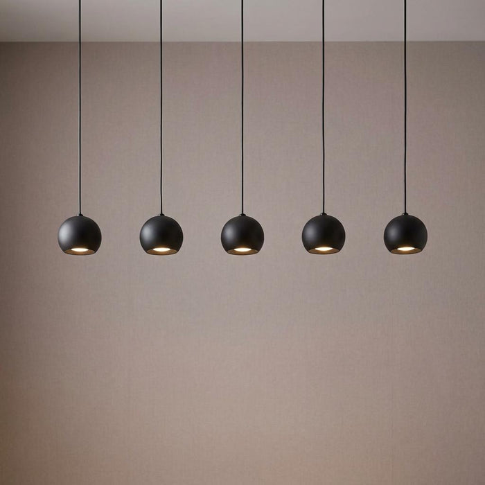 Five matt black spherical pendant lights hanging in a row against a beige wall.