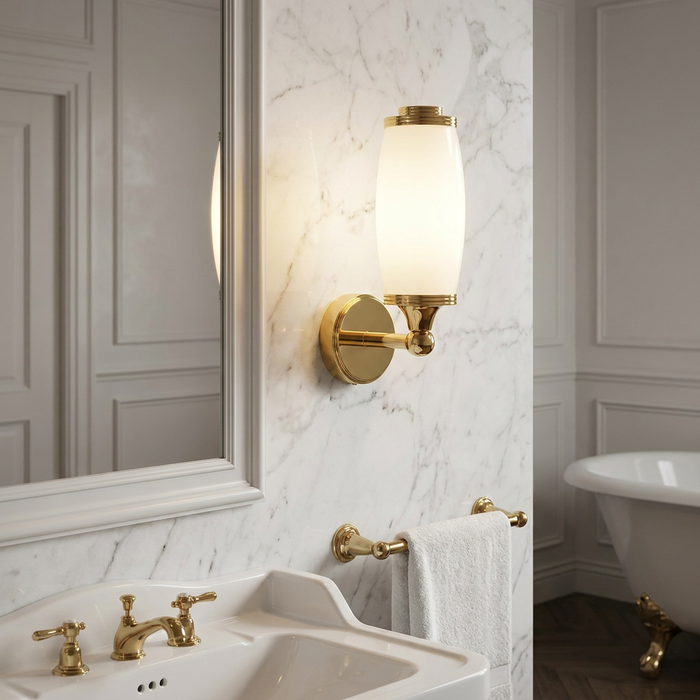 Polished brass wall light with a white glass shade mounted on a marble wall in a traditional bathroom.