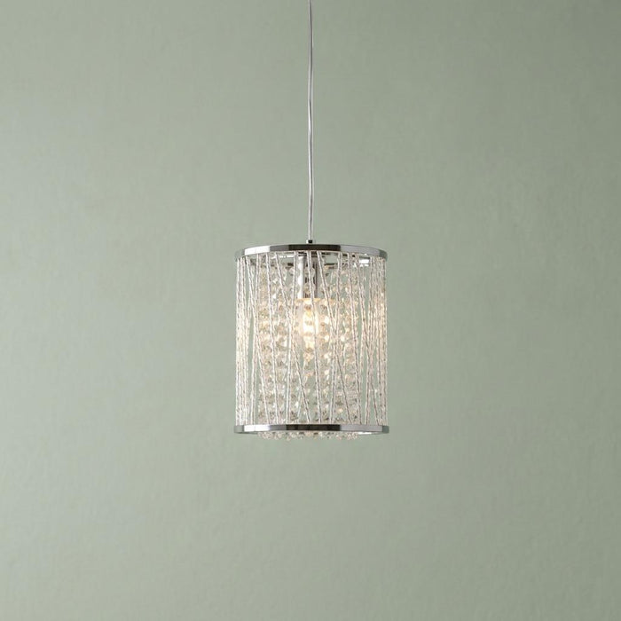 A chrome and crystal cylinder pendant light with glowing beads against a sage green wall.