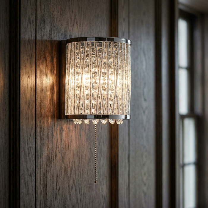Chrome and crystal wall light with a cord pull, glowing on dark wood paneling.