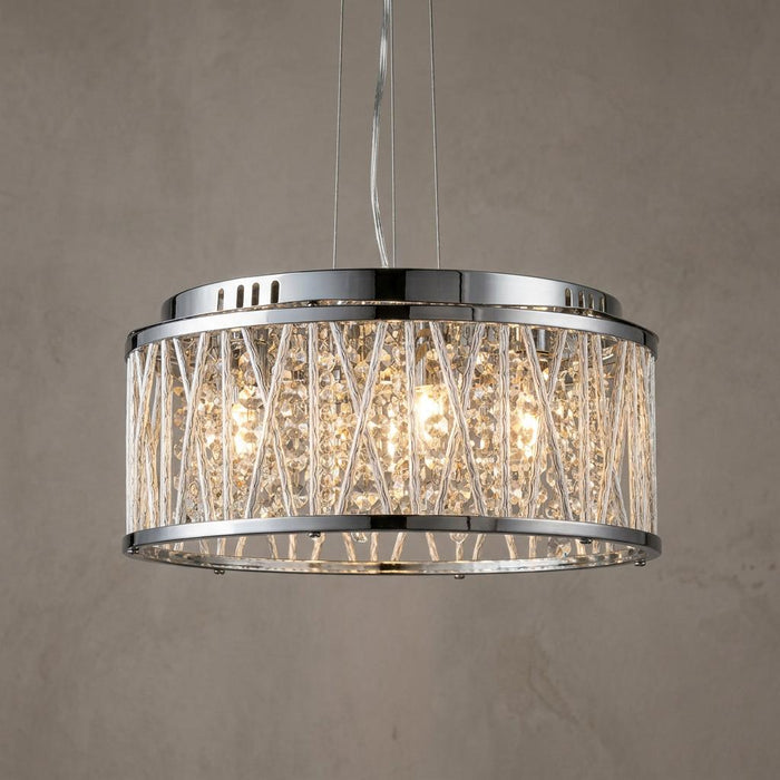 Drum-shaped chrome pendant light featuring crystal strands and a decorative cage, glowing against a neutral wall.