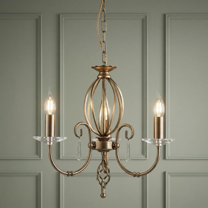 Elstead Aegean Aged Brass 3 Light Chandelier with crystal accents against a sage green paneled wall.