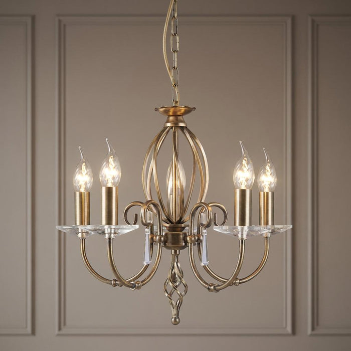 Elstead Aegean 5 light chandelier in aged brass with curved arms and glass droplets against a panelled wall.