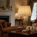 Elstead Aegean table lamp with pleated shade and brass cage base on a side table in a cozy living room.