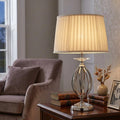 Elstead Aegean table lamp with polished nickel open base and pleated cream shade on a wooden side table.