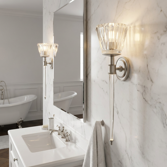 Brushed nickel bathroom wall light with fluted glass shade and long glass drop on a marble wall.