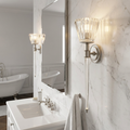 Brushed nickel bathroom wall light with fluted glass shade and long glass drop on a marble wall.