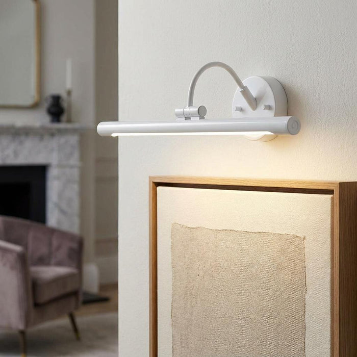 Modern white LED picture light mounted on a wall, illuminating a framed canvas in a living room.