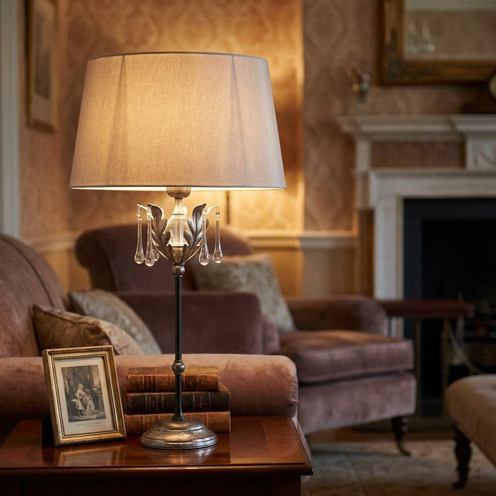 Elegant silver table lamp with crystal droplets and a cream shade on a wooden side table in a cozy living room.