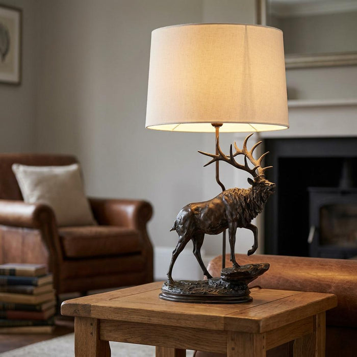 Bronze stag table lamp with a cream shade on a wooden table in a cozy living room.