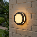 Circular black outdoor lantern with a warm light glow mounted on a white brick wall.